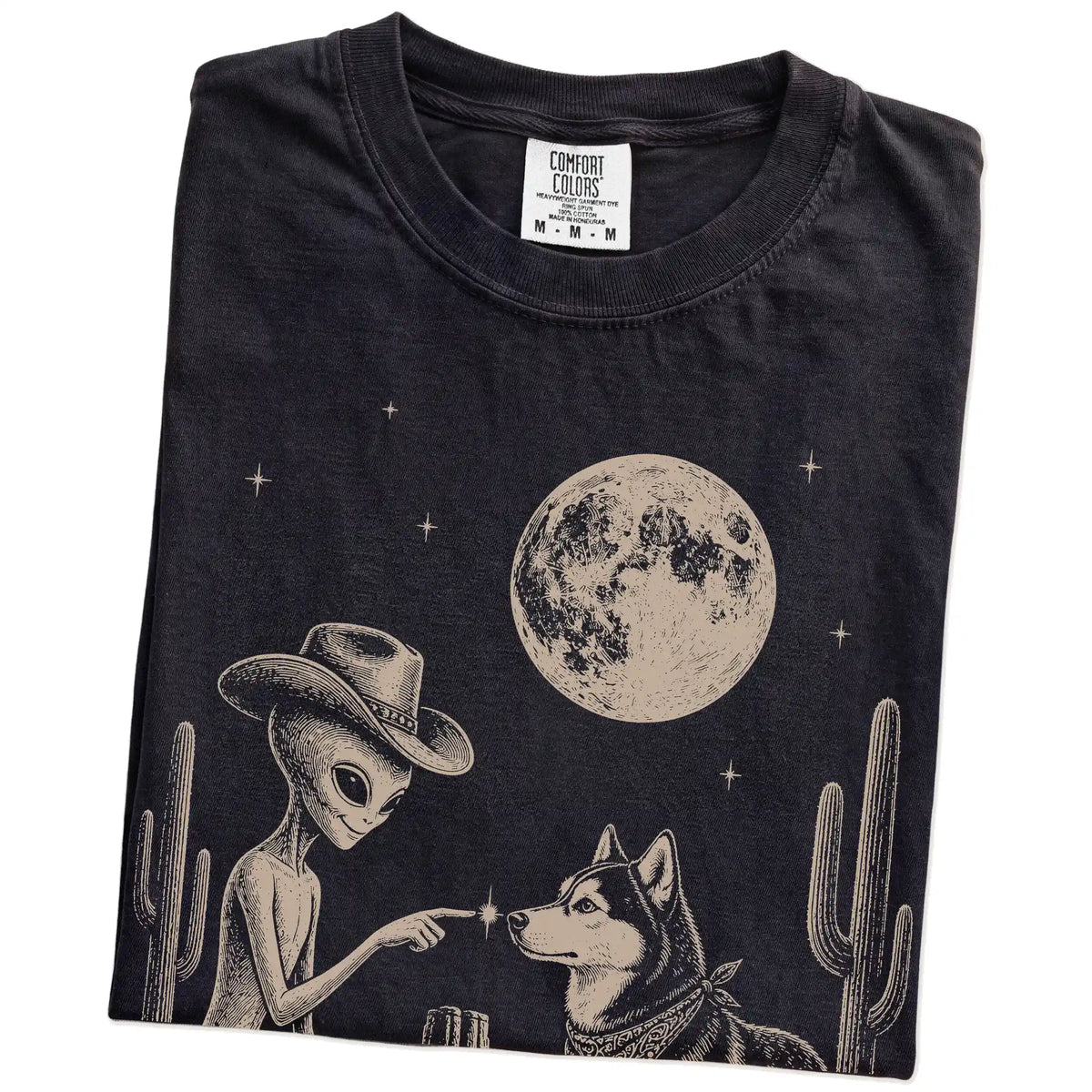 Folded Black Comfort Colors® T-shirt showing cowboy alien fist-bumping a husky beneath the moon
