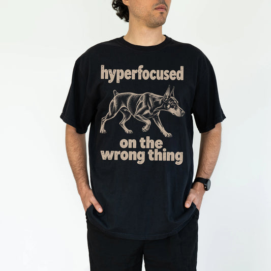 Person wearing a Black T-shirt with Doberman “hyperfocused on the wrong thing” design