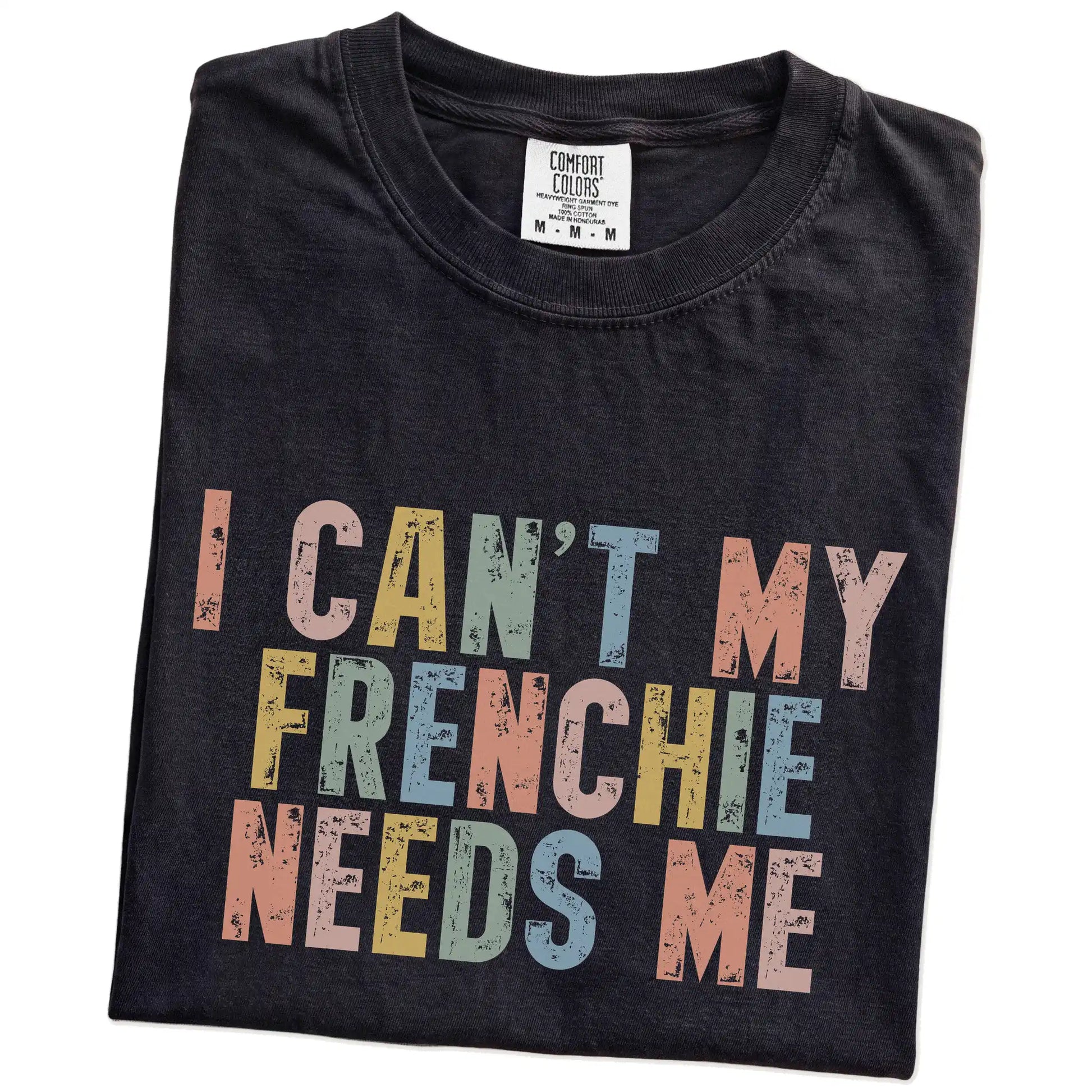 Folded Black Comfort Colors® T-shirt showing French Bulldog with “I Can’t, My Dog Needs Me” lettering