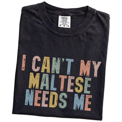 Folded Black Comfort Colors® T-shirt showing Maltese with “I Can’t, My Dog Needs Me” lettering