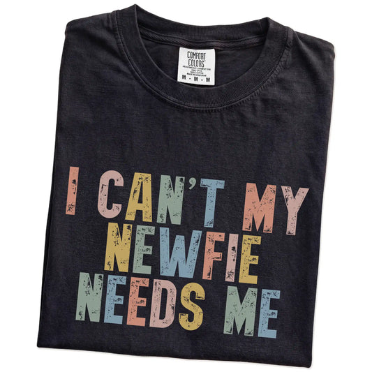 Folded Black Comfort Colors® T-shirt showing Newfie with “I Can’t, My Dog Needs Me” lettering