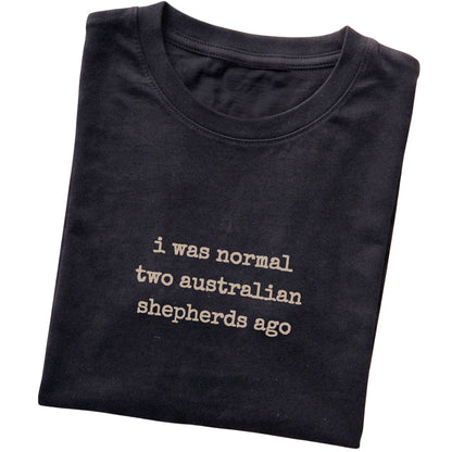 Black I Was Normal Two Australian Shepherds Ago T-shirt folded to show the printed design
