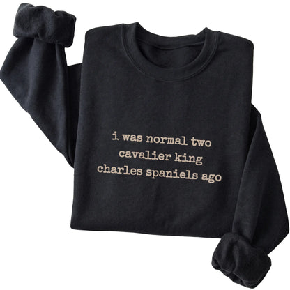 Black I Was Normal Two Cavalier King Charles Spaniels Ago sweatshirt folded to show the printed design