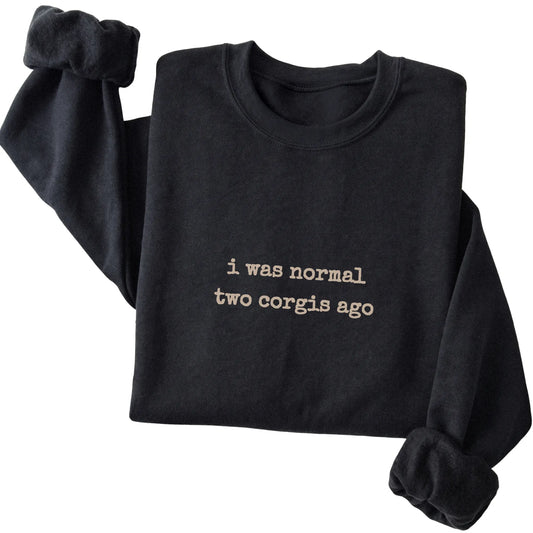 Black I Was Normal Two Corgis Ago sweatshirt folded to show the printed design