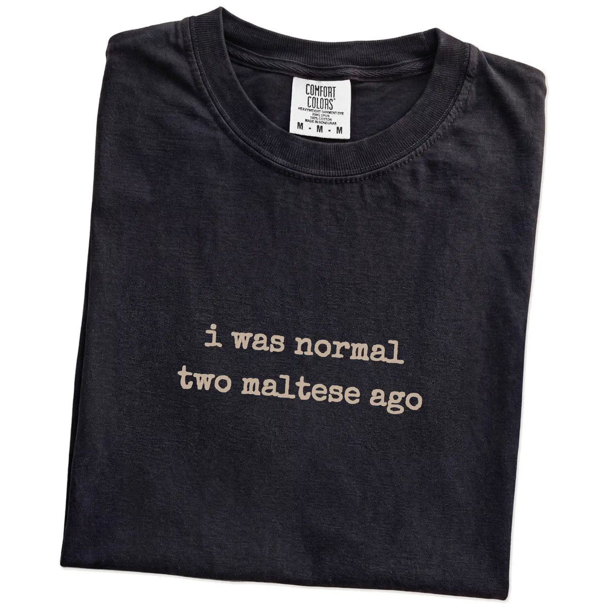 Folded Black Comfort Colors® T-shirt showing i was normal two maltese ago lettering