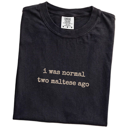 Folded Black Comfort Colors® T-shirt showing i was normal two maltese ago lettering
