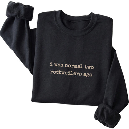 Black I Was Normal Two Rottweilers Ago sweatshirt folded to show the printed design