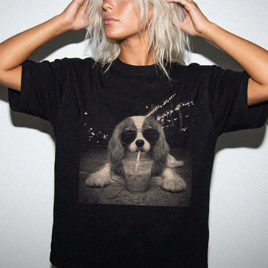 Model wearing a Black Comfort Colors® T-shirt featuring Cavalier King Charles Spaniel with iced coffee in a retro grunge desi