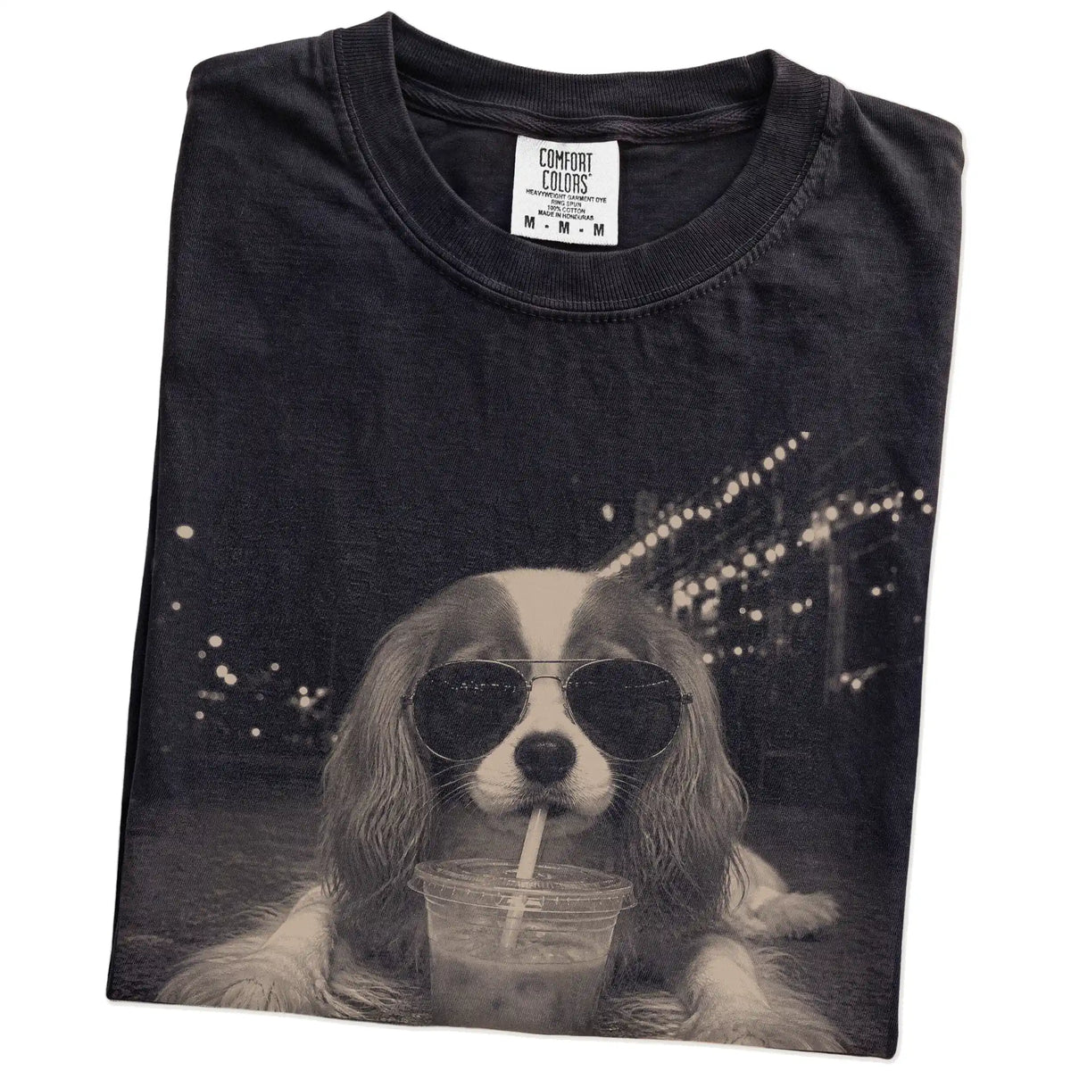 Folded Black Comfort Colors® T-shirt showing Cavalier King Charles Spaniel with iced coffee in a retro grunge design