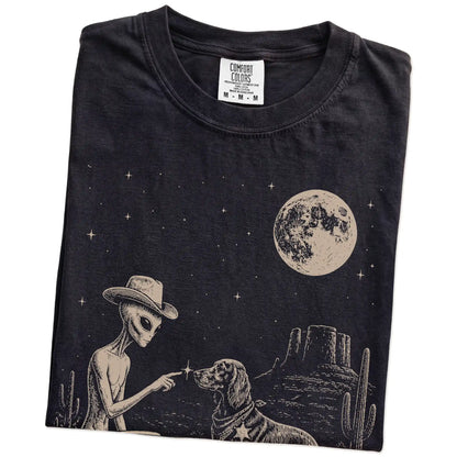 Folded Black Comfort Colors® T-shirt showing cowboy alien fist-bumping a irish setter beneath the moon