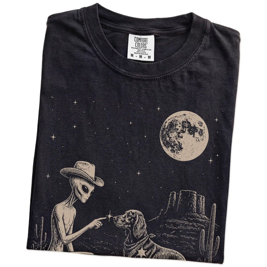 Folded Black Comfort Colors® T-shirt showing cowboy alien fist-bumping a irish setter beneath the moon