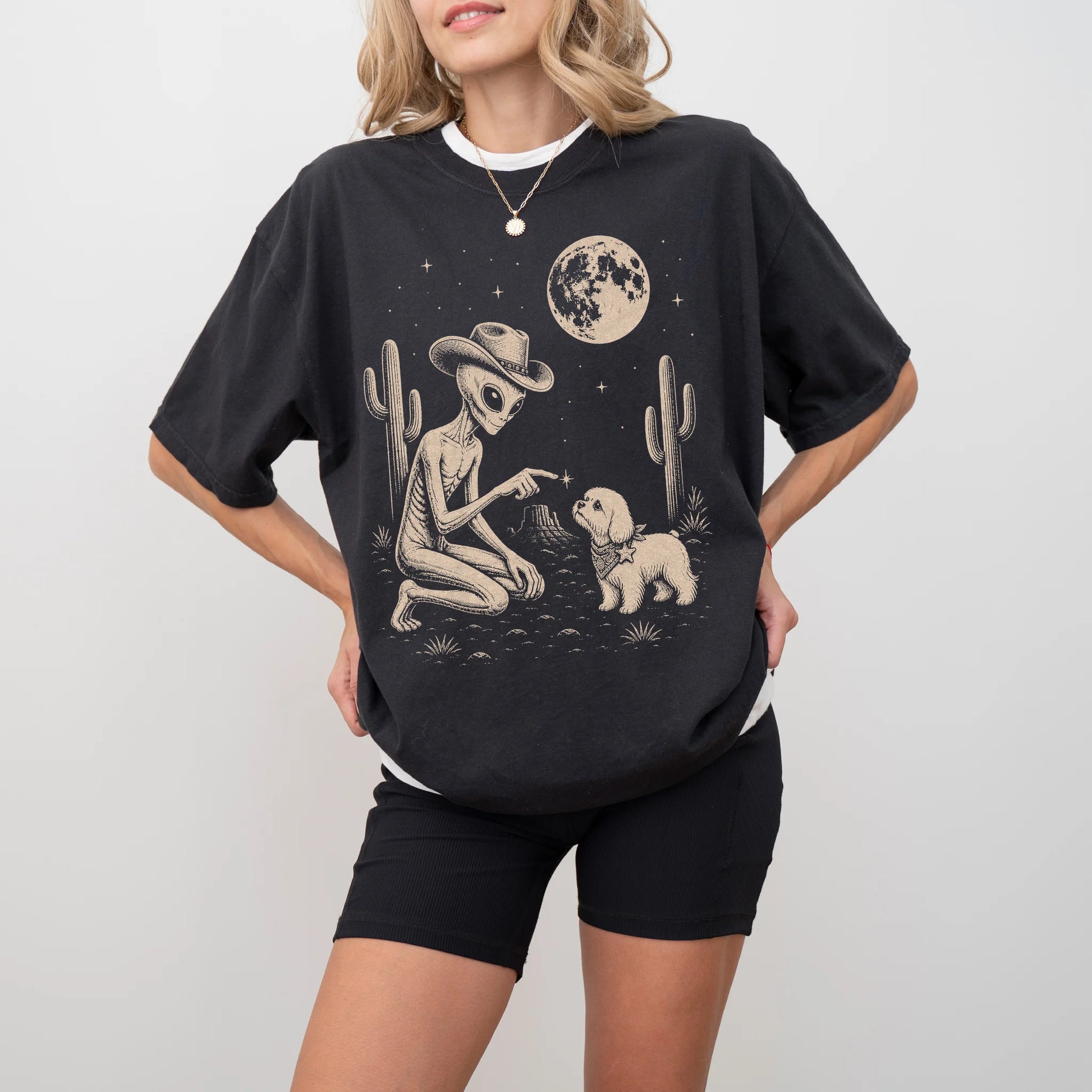 Model wearing a Black Comfort Colors® T-shirt with cowboy alien fist-bumping a maltese beneath the moon