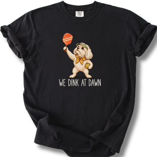 Maltese with a pickleball paddle and ball on a Black Comfort Colors® T-shirt with We Dink at Dawn text