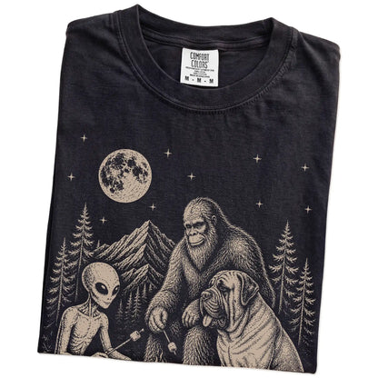 Folded Black Comfort Colors® T-shirt showing Mastiff camping with Bigfoot and an alien