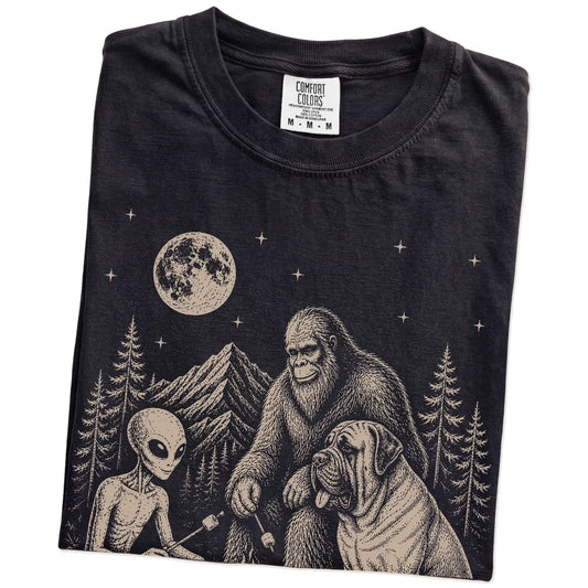 Folded Black Comfort Colors® T-shirt showing Mastiff camping with Bigfoot and an alien