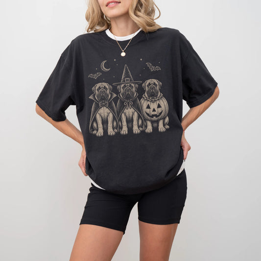 Model wearing a Black Comfort Colors® T-shirt showing three Mastiff dogs dressed for Halloween beneath bats and a crescent mo