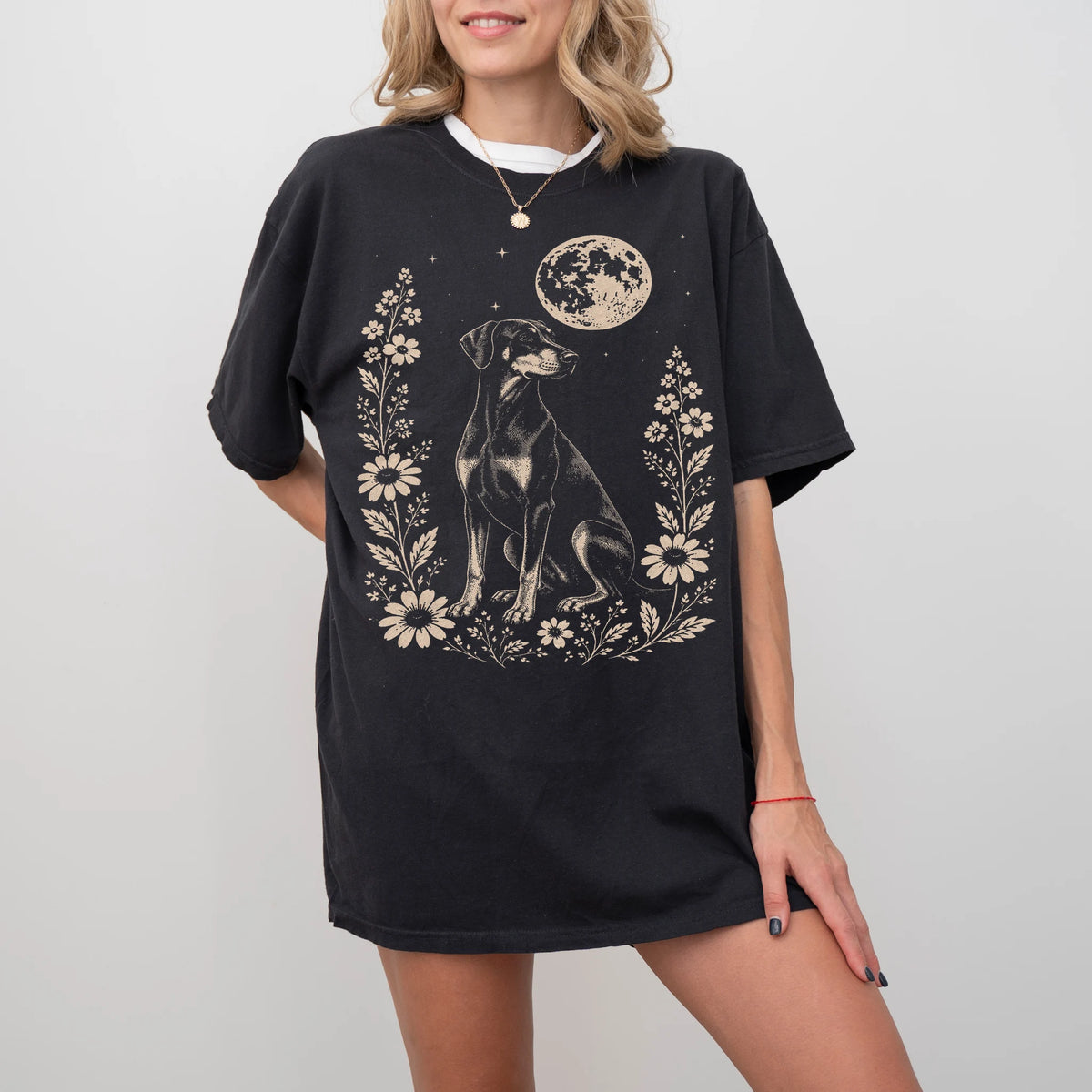 Model wearing a Black Comfort Colors® T-shirt featuring Doberman framed by flowers beneath the moon