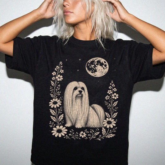 Model wearing a Black Comfort Colors® T-shirt featuring Maltese framed by flowers beneath the moon