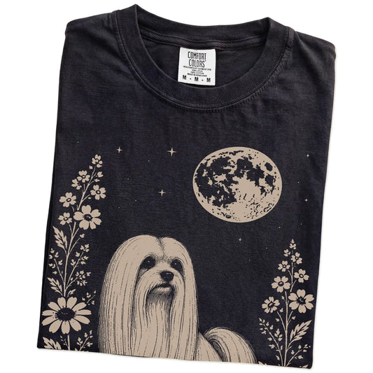 Folded Black Comfort Colors® T-shirt showing Maltese framed by flowers beneath the moon