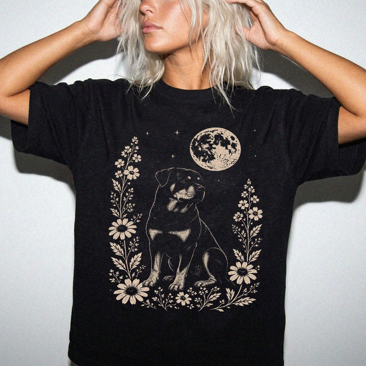Model wearing a Black Comfort Colors® T-shirt featuring Rottweiler framed by flowers beneath the moon