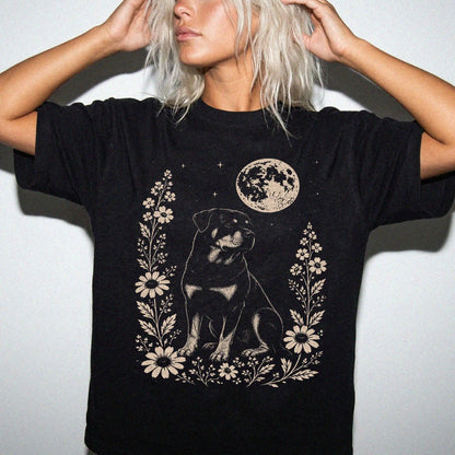 Model wearing a Black Comfort Colors® T-shirt featuring Rottweiler framed by flowers beneath the moon