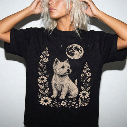 Model wearing a Black Comfort Colors® T-shirt featuring Westie framed by flowers beneath the moon