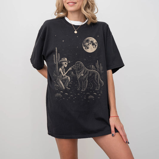 Model wearing a Black Comfort Colors® T-shirt with cowboy alien fist-bumping a newfie beneath the moon