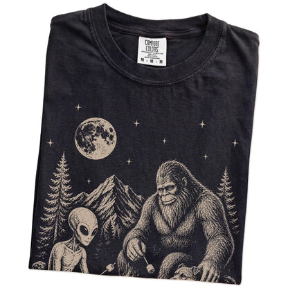 Folded Black Comfort Colors® T-shirt showing Pitbull camping with Bigfoot and an alien