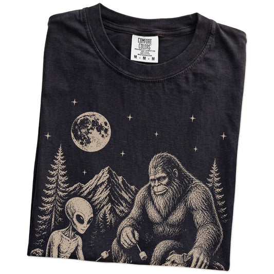Folded Black Comfort Colors® T-shirt showing Pitbull camping with Bigfoot and an alien