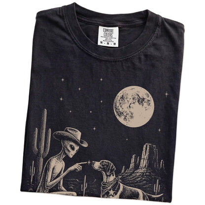 Folded Black Comfort Colors® T-shirt showing cowboy alien fist-bumping a pointer beneath the moon
