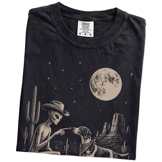 Folded Black Comfort Colors® T-shirt showing cowboy alien fist-bumping a pointer beneath the moon