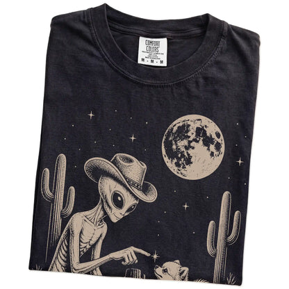 Folded Black Comfort Colors® T-shirt showing cowboy alien fist-bumping a pomeranian beneath the moon