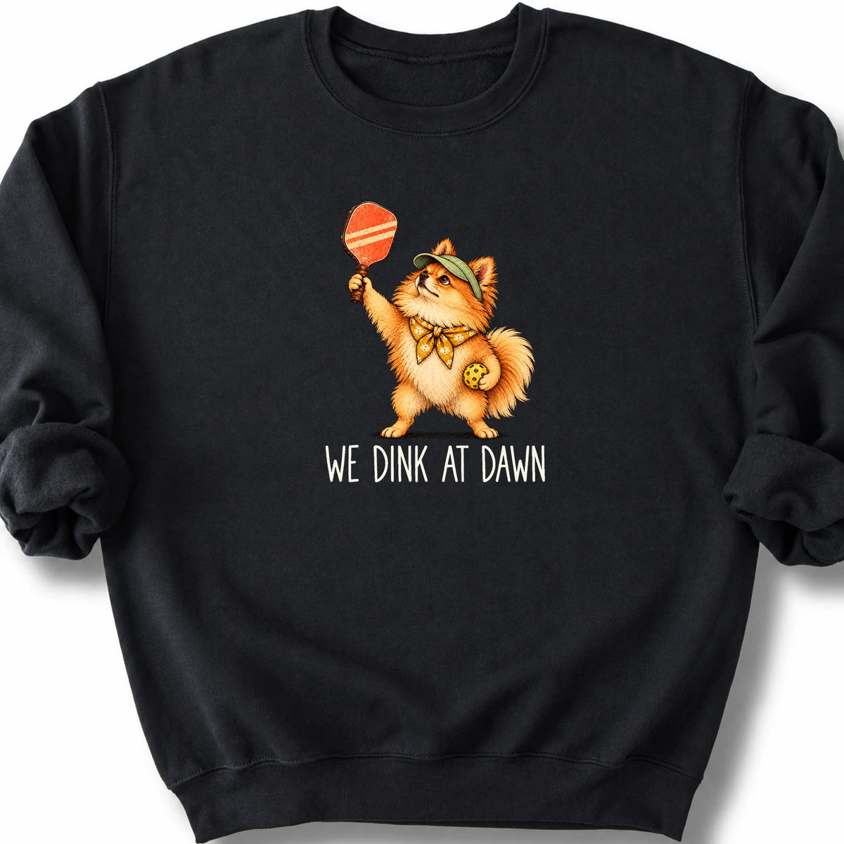 Pomeranian with a pickleball paddle and ball on a Black Gildan® sweatshirt with We Dink at Dawn text