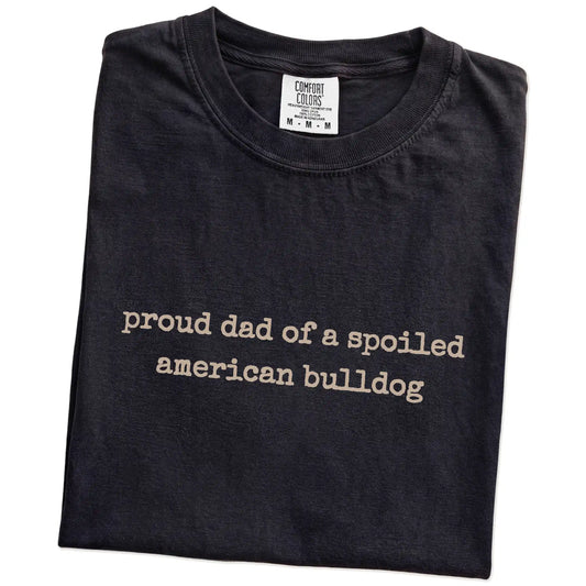 Folded Black Comfort Colors® T-shirt showing proud dad of a spoiled american bulldog lettering
