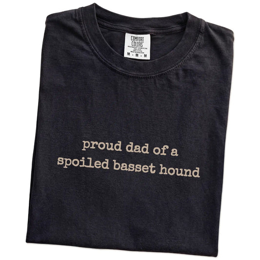Folded Black Comfort Colors® T-shirt showing proud dad of a spoiled basset hound lettering