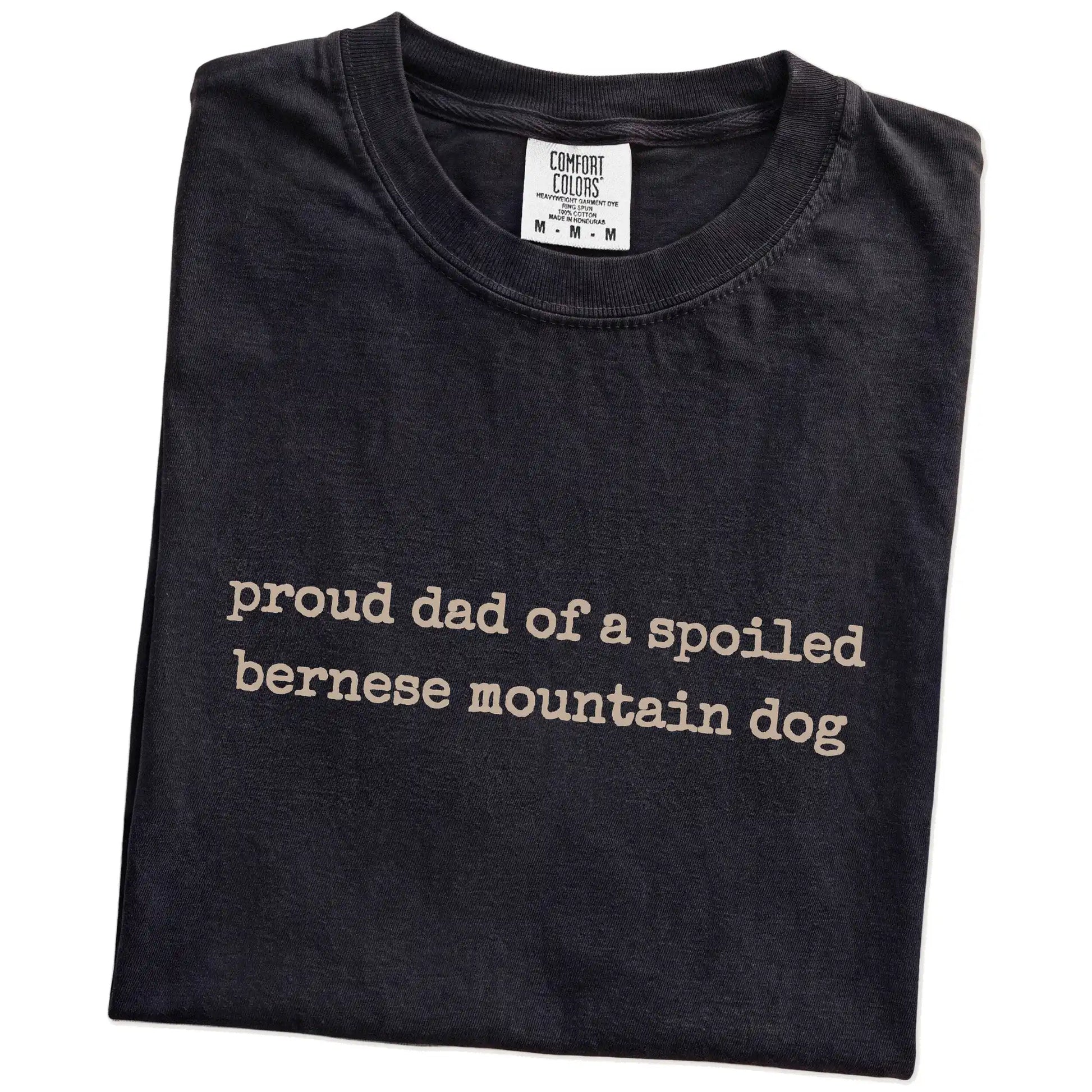 Folded Black Comfort Colors® T-shirt showing proud dad of a spoiled bernese mountain dog lettering