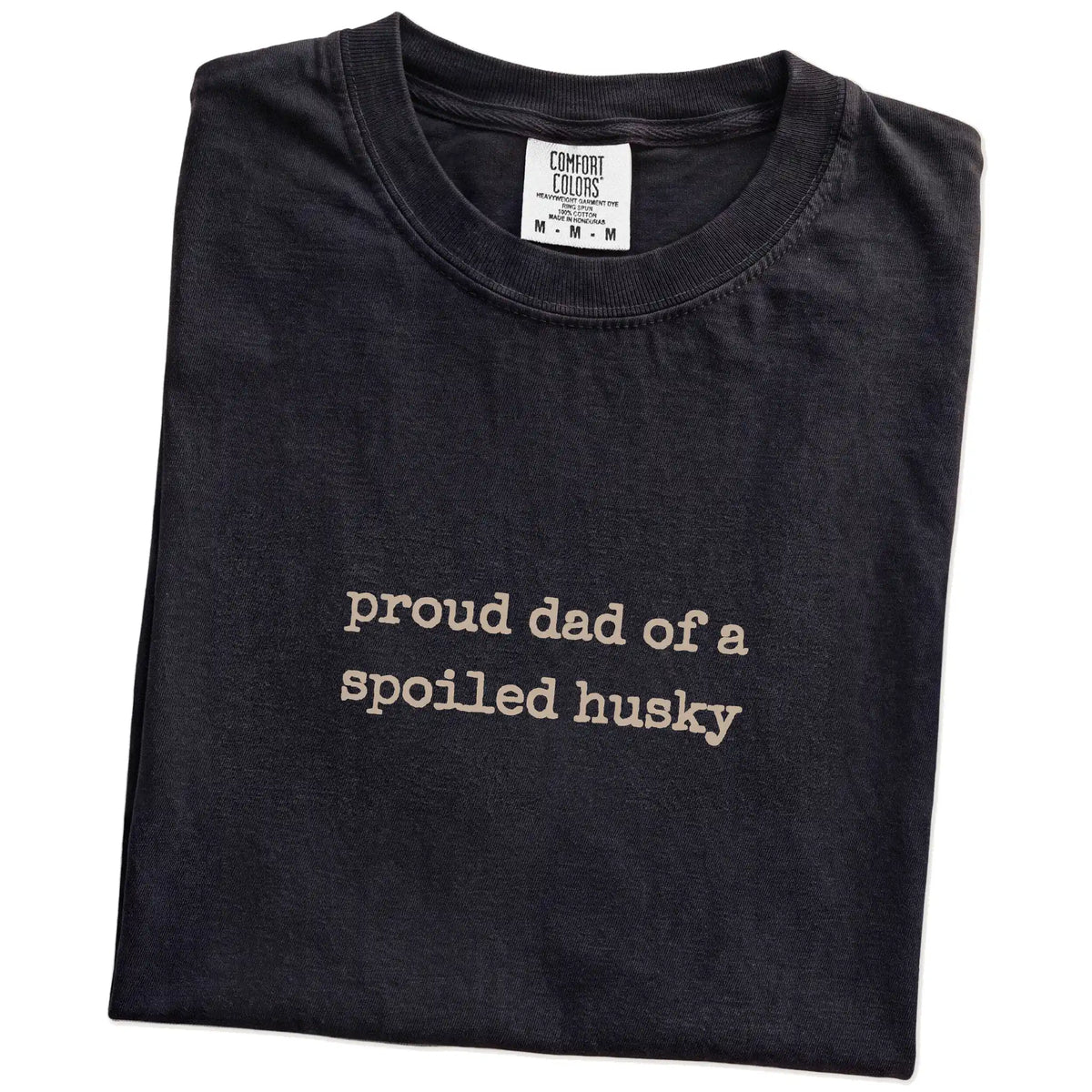 Folded Black Comfort Colors® T-shirt showing proud dad of a spoiled husky lettering