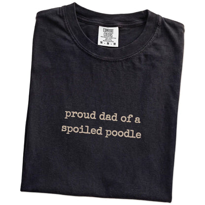 Folded Black Comfort Colors® T-shirt showing proud dad of a spoiled poodle lettering