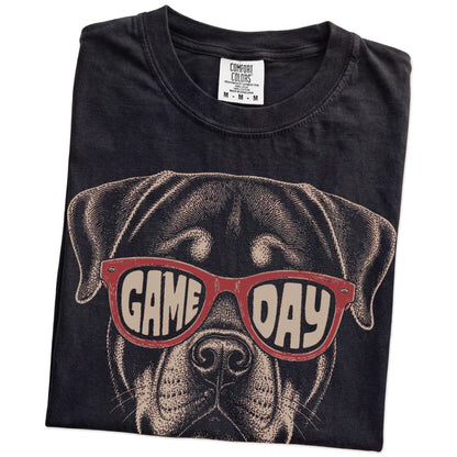 Folded Black Comfort Colors® T-shirt showing rottweiler wearing red game day sunglasses