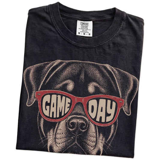 Folded Black Comfort Colors® T-shirt showing rottweiler wearing red game day sunglasses