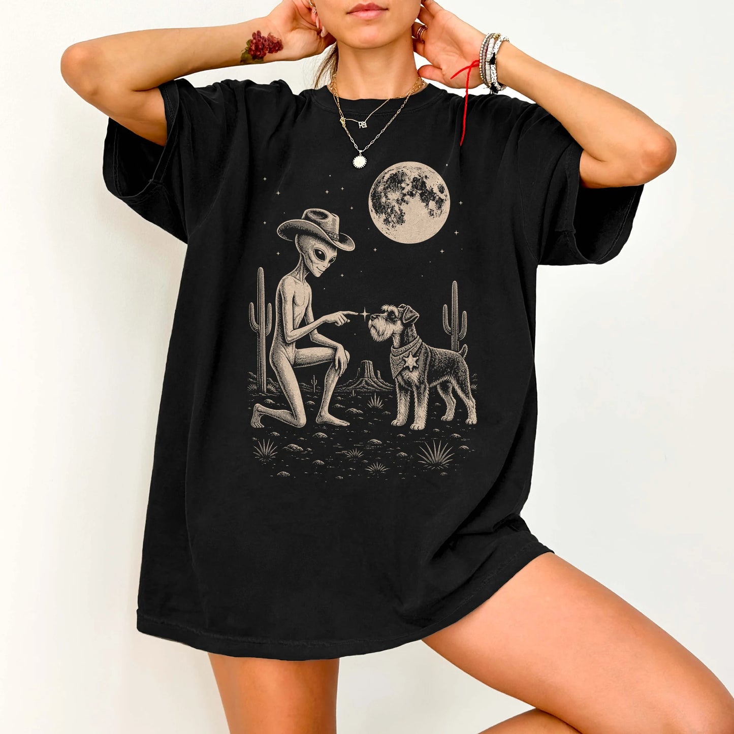 Model wearing a Black Comfort Colors® T-shirt with cowboy alien fist-bumping a schnauzer beneath the moon
