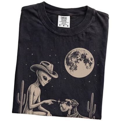 Folded Black Comfort Colors® T-shirt showing cowboy alien fist-bumping a schnauzer beneath the moon