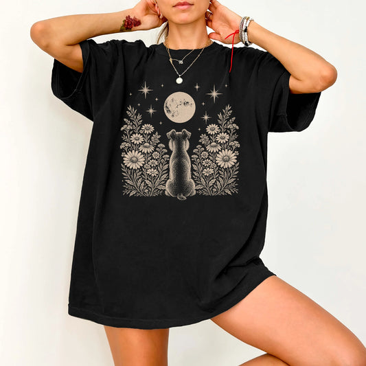 Model wearing a Black Comfort Colors® T-shirt featuring Schnauzer beneath a wildflower moon