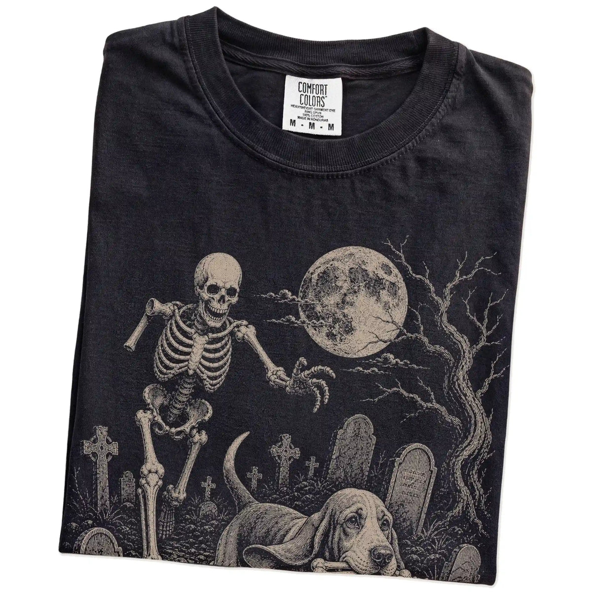Folded Black Comfort Colors® T-shirt showing Basset Hound running through a moonlit graveyard with a chasing skeleton