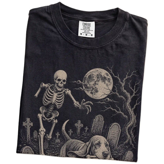 Folded Black Comfort Colors® T-shirt showing Basset Hound running through a moonlit graveyard with a chasing skeleton
