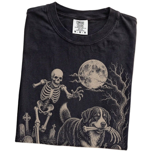 Folded Black Comfort Colors® T-shirt showing Bernese Mountain Dog running through a moonlit graveyard with a chasing skeleton