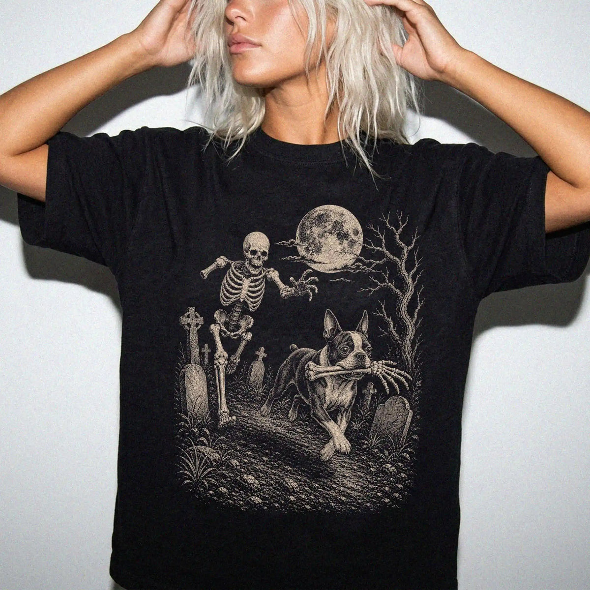 Model wearing a Black Comfort Colors® T-shirt showing Boston Terrier running through a moonlit graveyard with a chasing skele