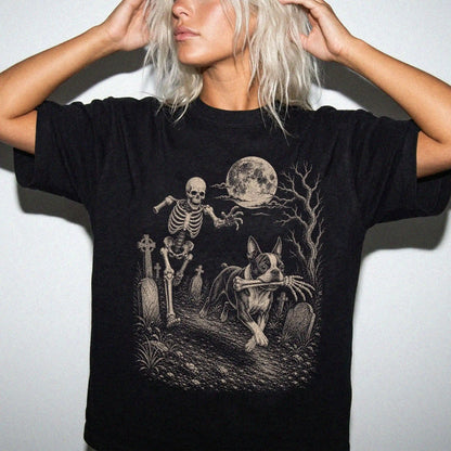 Model wearing a Black Comfort Colors® T-shirt showing Boston Terrier running through a moonlit graveyard with a chasing skele