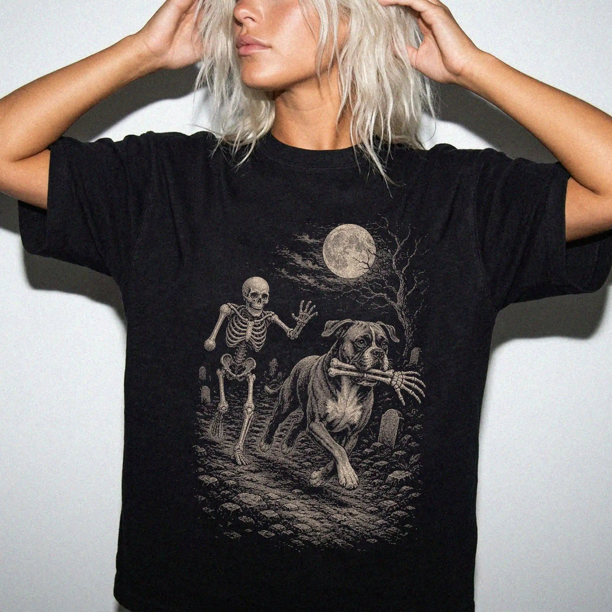 Woman wearing a black T-shirt with a Boxer carrying a skeleton arm through a graveyard.