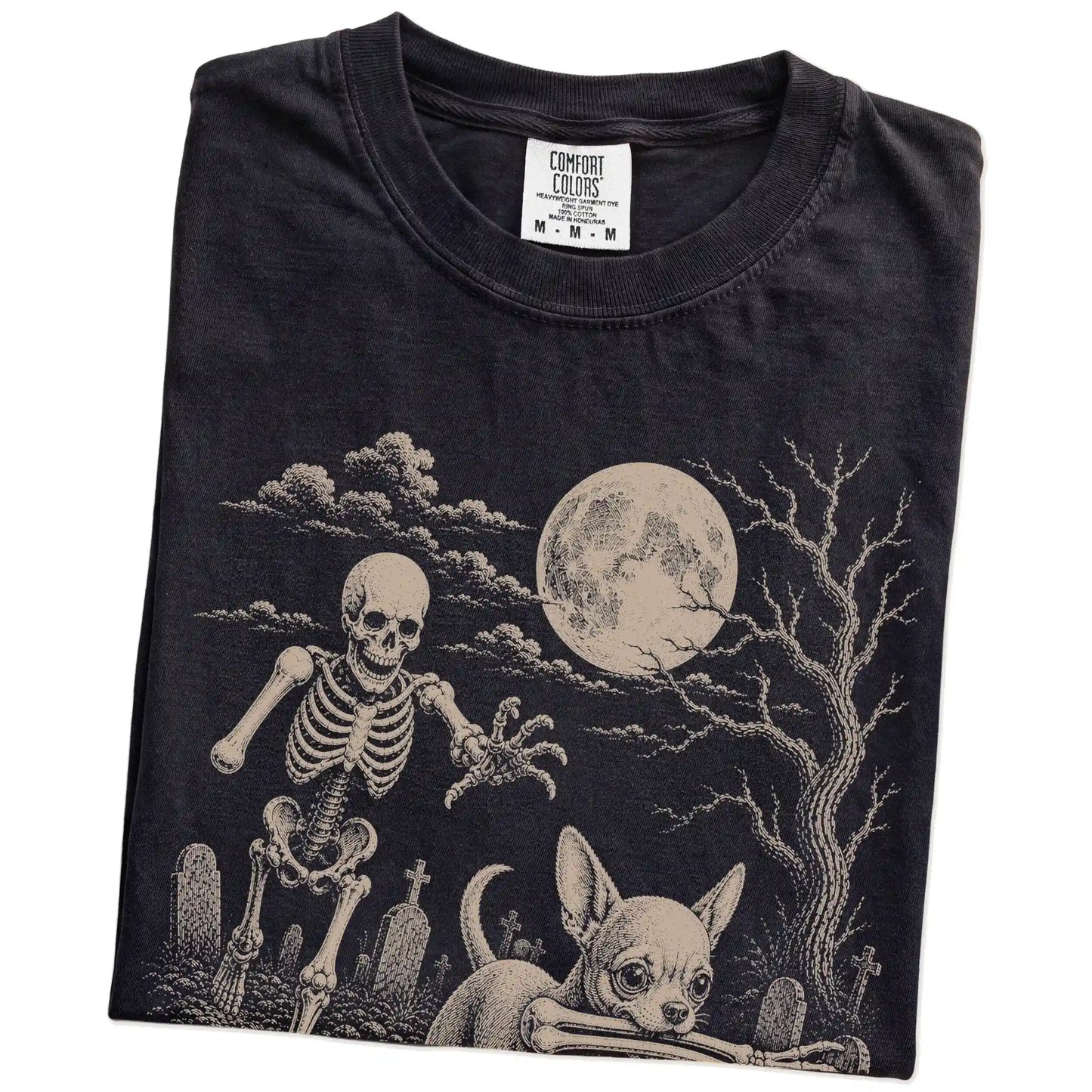 Folded Black Comfort Colors® T-shirt showing Chihuahua running through a moonlit graveyard with a chasing skeleton